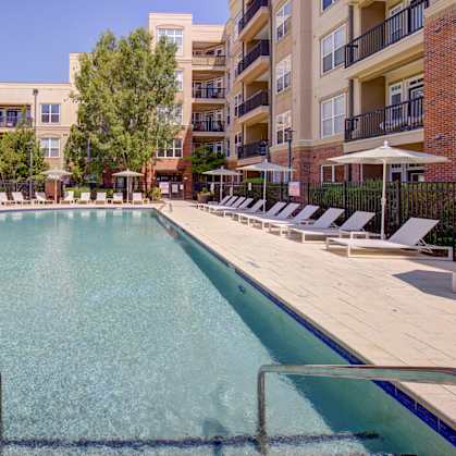 A large swimming pool surrounded by sun loungers and apartment buildings.