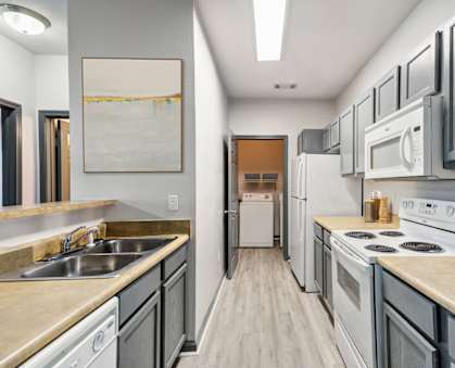 Parc at Metro Center Apartments near Buena Vista Heights, TN photo of a long kitchen with white appliances and wooden floors and Grey Cabinets