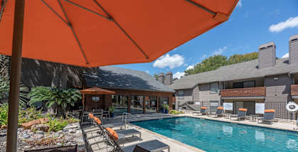 Fusion 35 Apartments pool area with a table and chairs under an orange umbrella.