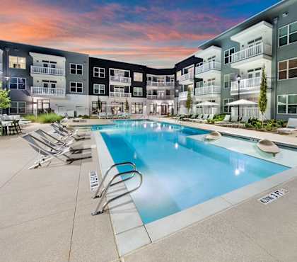 A swimming pool surrounded by lounge chairs in front of apartment buildings at The Barrett in Kennesaw, GA