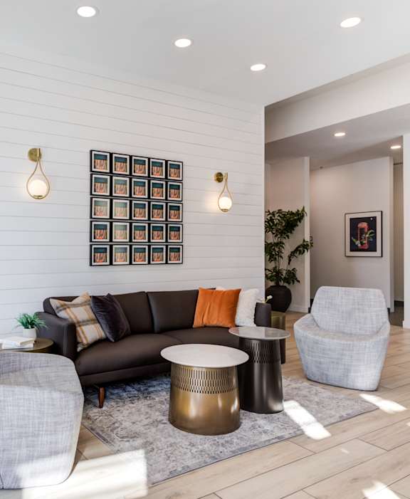 A modern living room with a grey sofa, a grey armchair, a black cabinet, and a wooden floor.