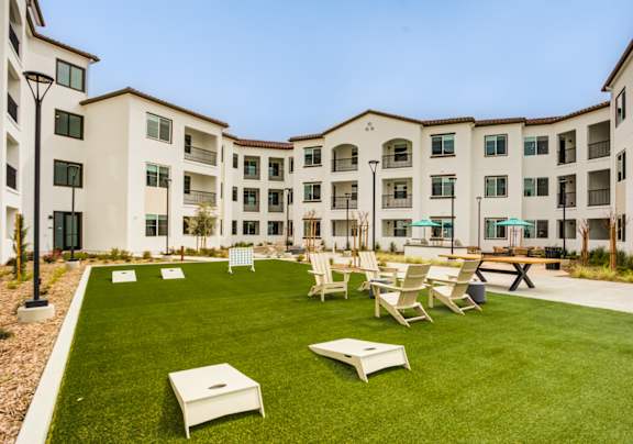 A large grassy area with chairs and tables in front of apartment buildings at Pradera Apartments, San Ramon, California