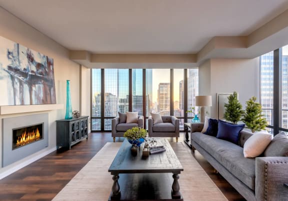 The living room with a couch, plush chairs, coffee table, decorations, a TV, and floor to ceiling windows showing the skyline of Minneapolis at NIC on 5th Apartments. 