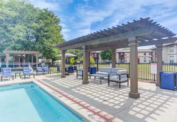 A pool area with a pergola and lounge chairs.