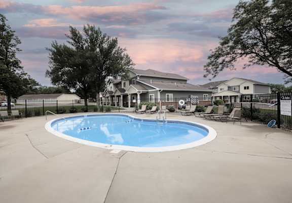 A large outdoor swimming pool surrounded by a fence and a house in the background.