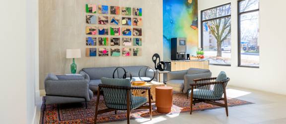A living room with a grey couch, a green chair, a brown table and a wall with pictures.
