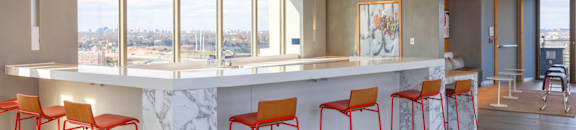 A row of red bar stools are lined up in front of a marble counter.
