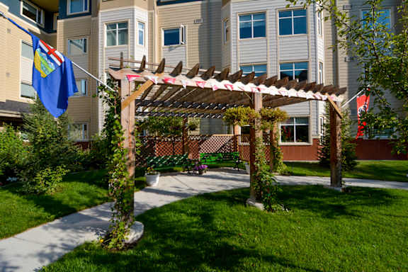 A building with a flag on the left and a pergola in the middle of a grassy area.