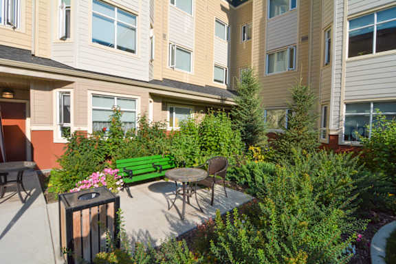 A patio with a table and chairs surrounded by green plants.
