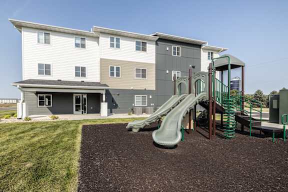 A playground with a green slide and a brown wooden structure.
