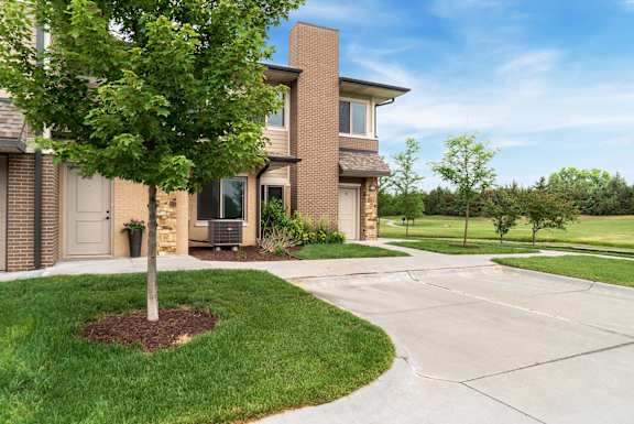a tree in front of an apartment with driveway and sidewalk
