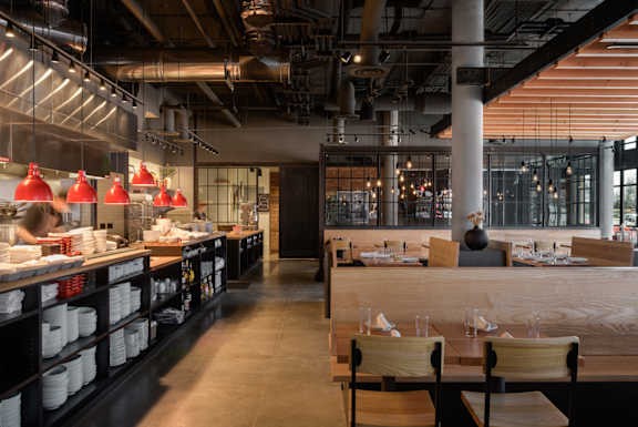 the interior of a restaurant with wooden tables and chairs and a bar with a counter at The Lucy Boise Apartments, Idaho, 83702