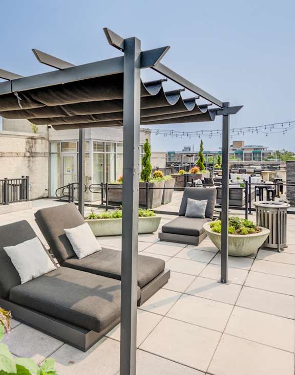 A patio with a black sofa and a black table under a black pergola.