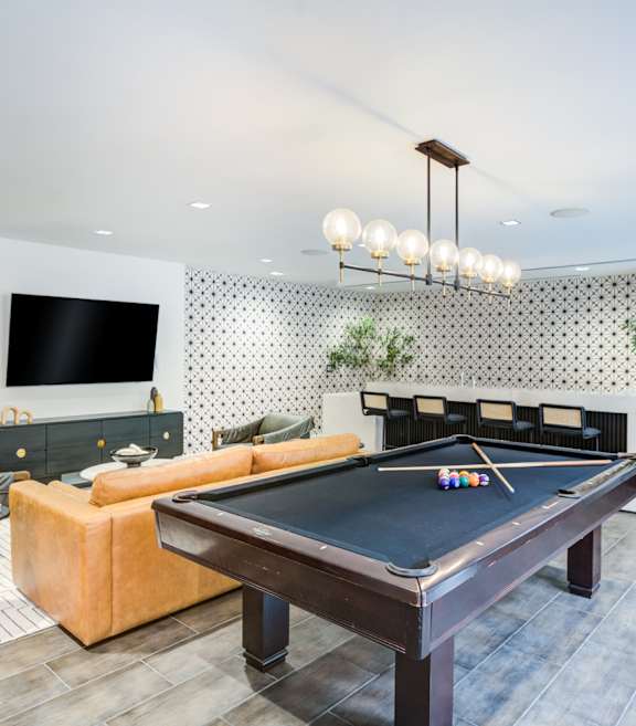 A pool table is in the middle of a room with a couch and a television.