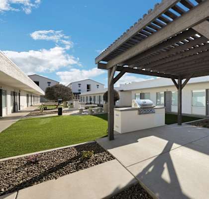 a covered patio with a grill and a lawn in front of a building