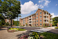 Exterior View of Claremont on the Square 4-story apartment buildings in Exton, PA with nearby resident parking and beautiful trees and flowers.