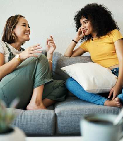 Two women are sitting on a couch having a conversation.