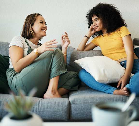 Two women are sitting on a couch having a conversation.