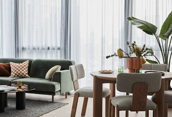 A modern living room with a green couch, a coffee table, and a dining table set for two.
