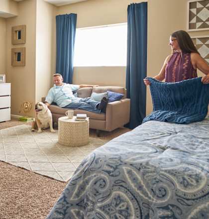 A woman holding a blue blanket in a room with a man sitting on a couch. at The Winhall of Williams Pointe Apartments, Waukee