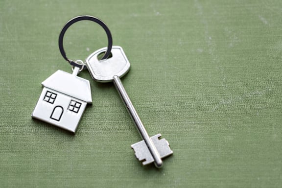 A key with a house-shaped keychain is lying on a green surface.