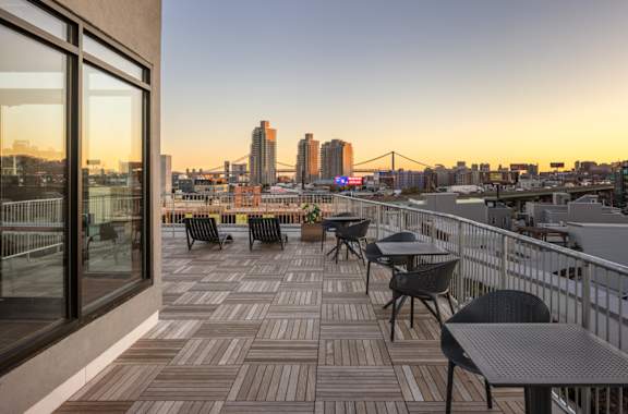 a balcony with tables and chairs overlooking a city at sunset