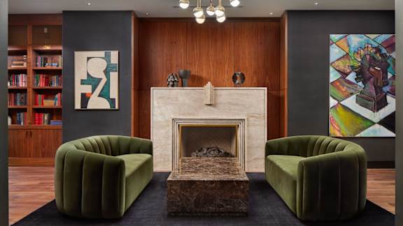 A living room with a fireplace, two green chairs, and a bookshelf.