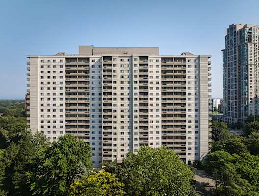 A large white building with many windows is surrounded by trees.