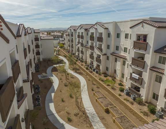 A row of apartment buildings with a sidewalk and landscaping in front.
