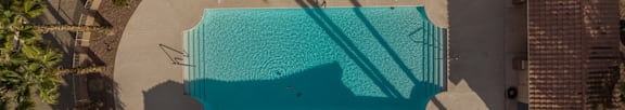 An aerial view of a swimming pool surrounded by palm trees and a building.