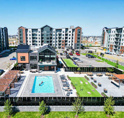 A large swimming pool is surrounded by a grassy area and a building with a red roof.