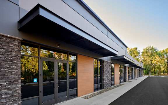 The image shows a modern building with a stone pillar on the left and a row of glass doors with numbers on them.