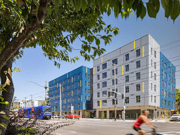 A cyclist is riding on a street in front of a blue and grey building.