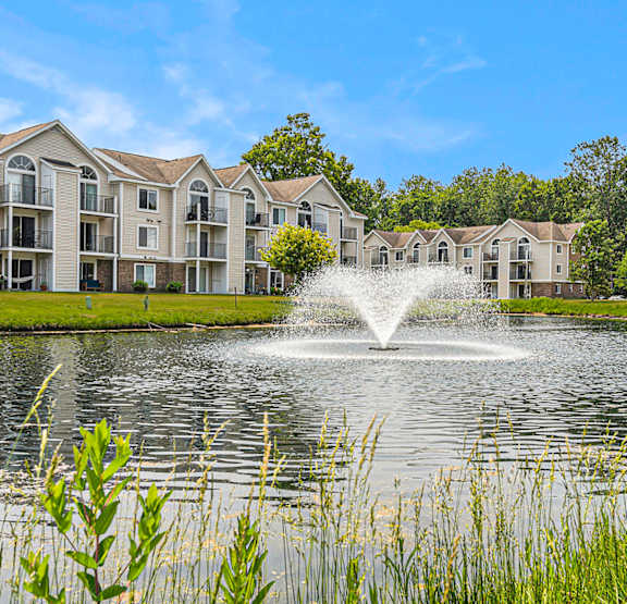 A fountain in the middle of a lake in front of apartment buildings at Orchard Lakes Apartments in Toledo, OH