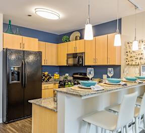 A kitchen with a black refrigerator, wooden cabinets, and a dining table set for two.