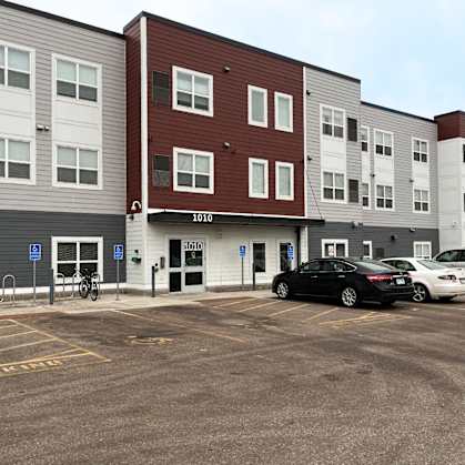 A parking lot in front of a multi-story apartment building with a black car parked in the lot.