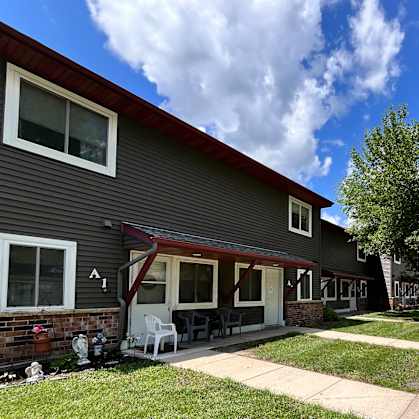 A house with a grey siding and a red roof with a patio and a tree in front.