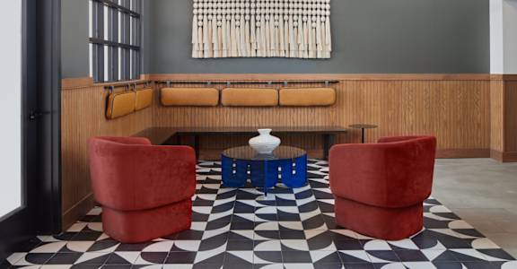 A black and white checkered floor with a red chair and a blue table in front of a wooden bench. at The Weaver, Philadelphia