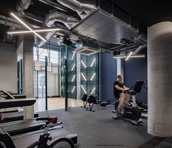 A man is working out on a stationary bike in a gym with a concrete column and a row of treadmills.