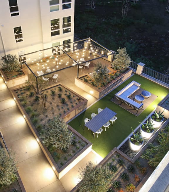 A rooftop garden with a table and chairs is lit up at night.