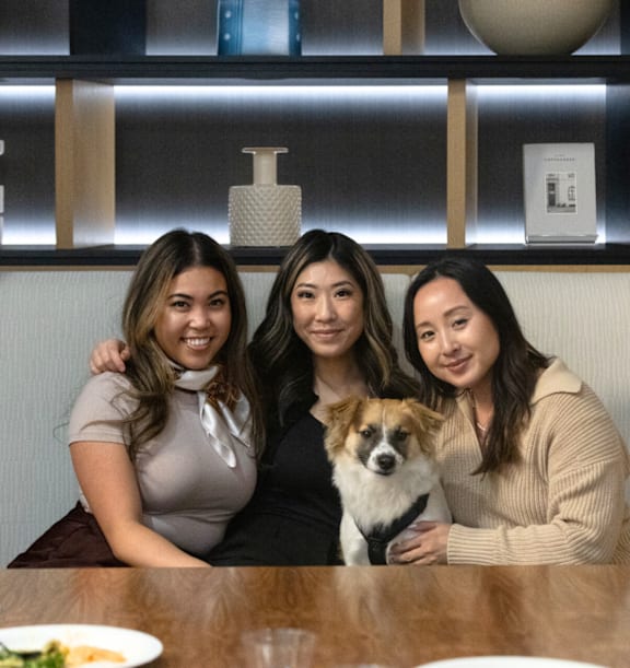 Three women and a dog are sitting at a table.