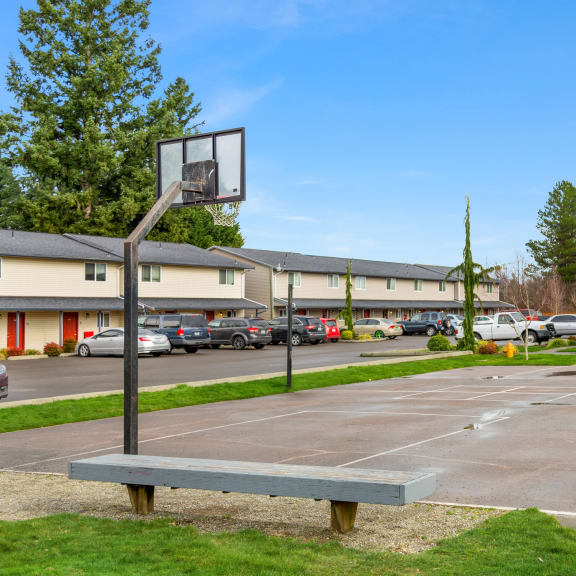 Outdoor basketball court with two hoops opposite each other, surrounded by grass, a bench, a picnic table, and trees.at Quilceda Gardens, Marysville