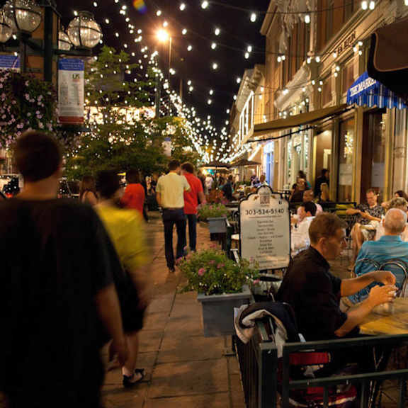 A busy street scene with people walking and sitting at tables.