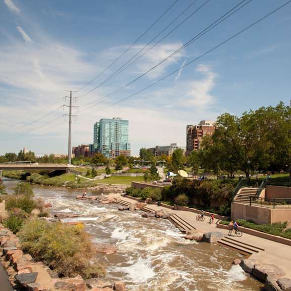 A river flows through a city park with people riding bikes on the path.