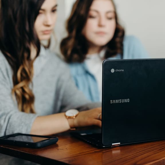 two women sitting at a table with a laptop computer
