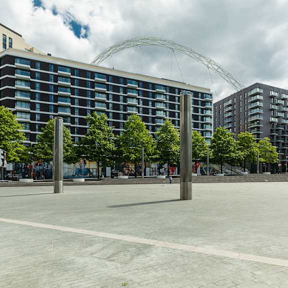 A large building with a glass facade is surrounded by trees and a large metal structure in the background.