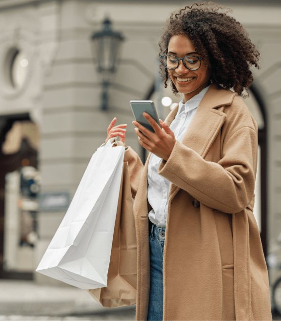 a woman looking at her cell phone while holding a shopping bag