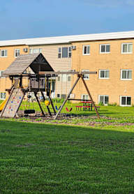 A playground with a swing set and slide in front of a building.