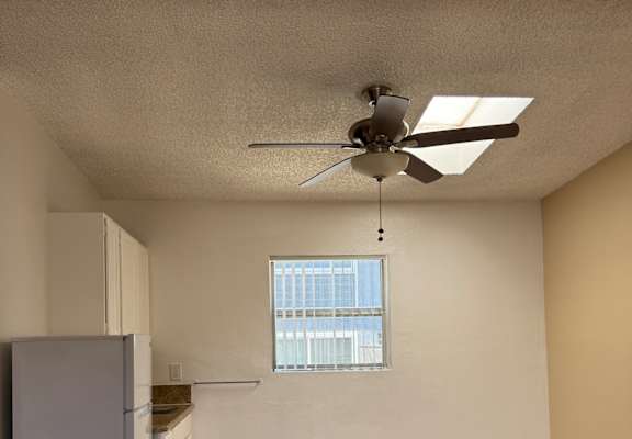 A bedroom with a bed, a fan, and a window.