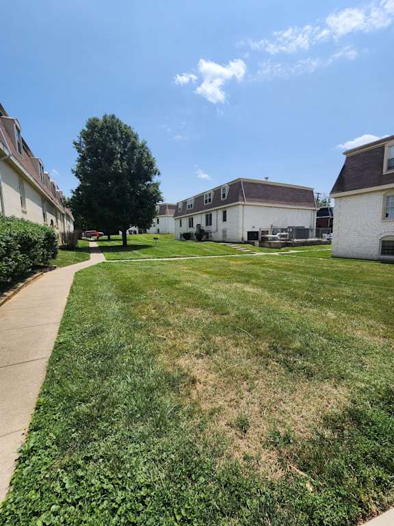 A grassy area with a sidewalk and a few buildings in the background.